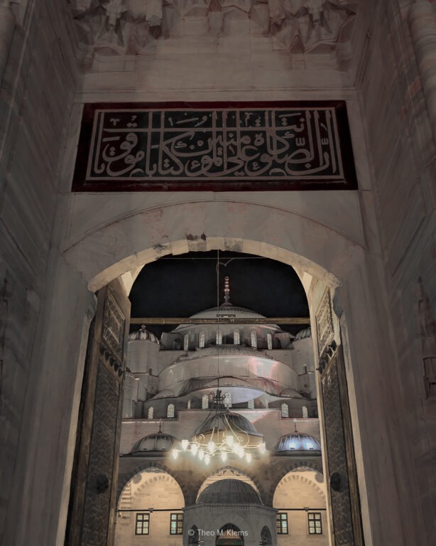 Blick durch ein Tor in den Innenhof einer Moschee mit Kuppeln und Licht in Istanbul