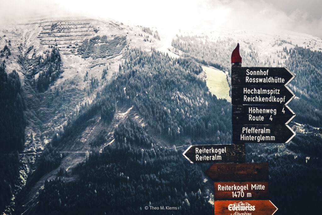 Wegweiser auf einem Wanderweg oberhalb von Viehhofen mit Blick in die Berge