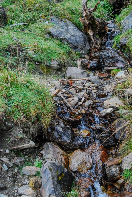 Kleiner Bergbach fließt zwischen Steinen entlang eines Wanderwegs
